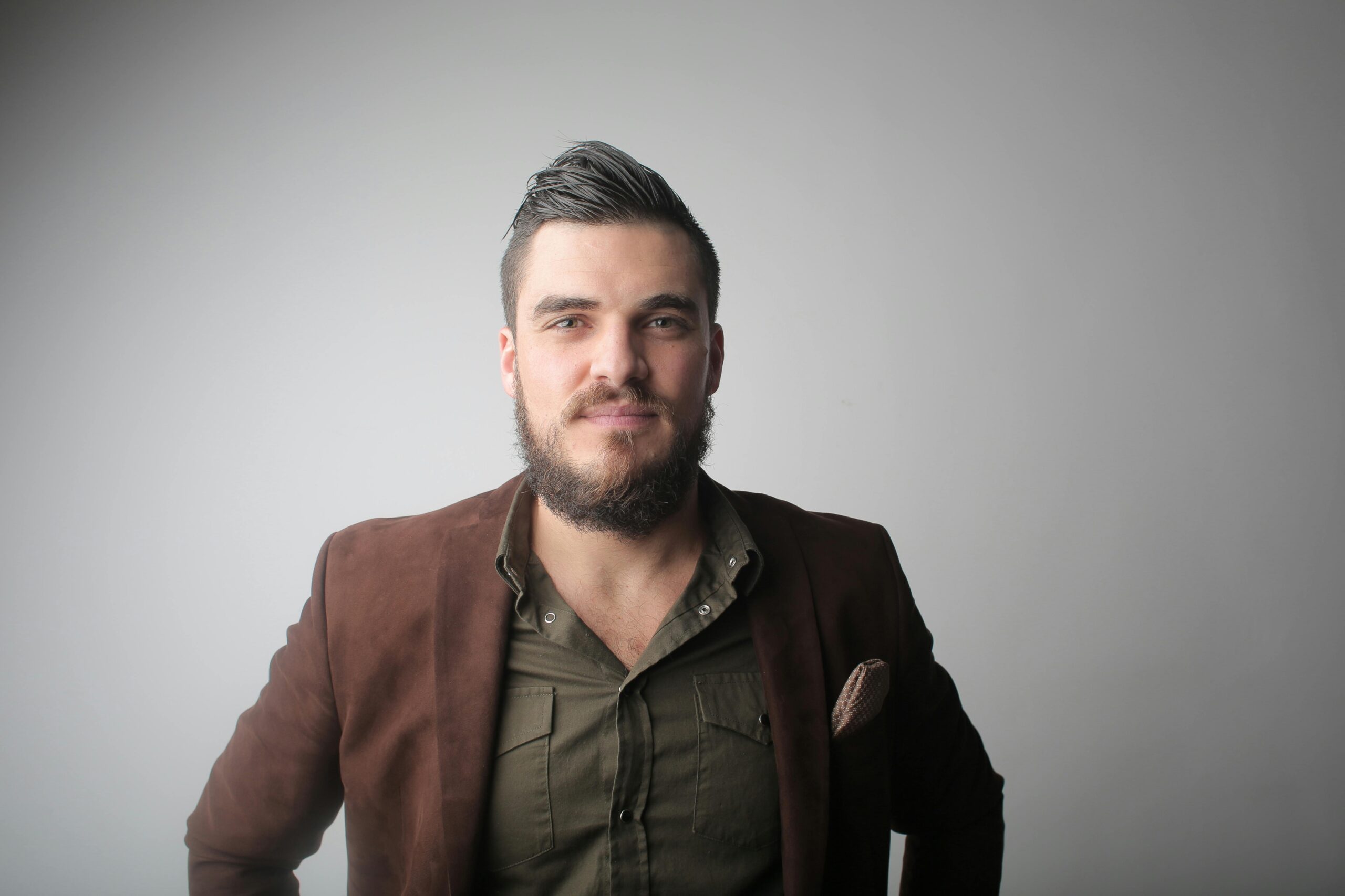 Close-up portrait of a bearded man in a stylish jacket, photographed in a studio setting.